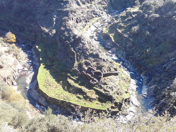 A rugged landscape with a circular stone structure surrounded by steep cliffs and sparse vegetation.