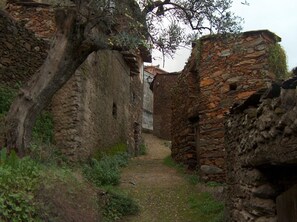 A narrow stone pathway flanked by rustic stone walls, leading to a traditional building with a tiled roof. - Sabores Hurdanos (Ladrillar)