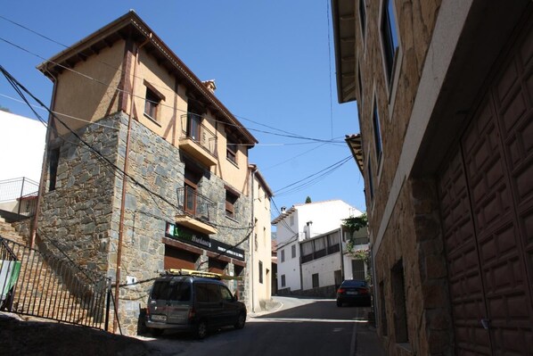 Una calle estrecha con edificios de piedra, una furgoneta estacionada y un coche.