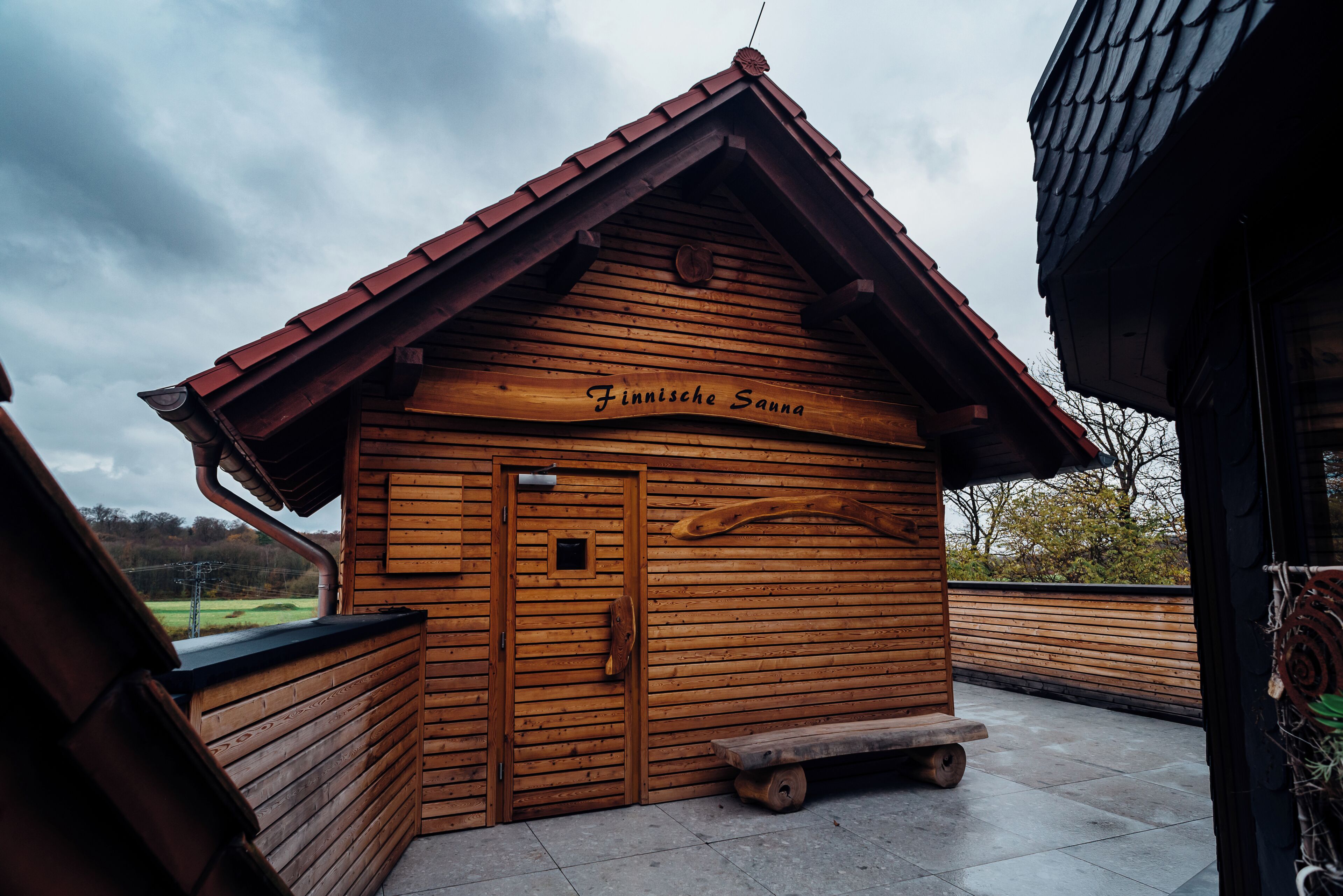 Una baita in legno con tetto spiovente, una panchina all'esterno e un cartello con scritto 'Finnische Sauna'.