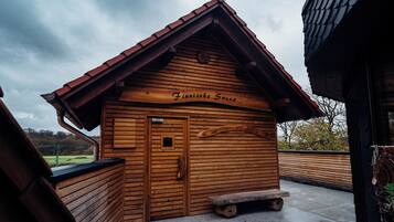 Una baita in legno con tetto spiovente, una panchina all'esterno e un cartello con scritto 'Finnische Sauna'.