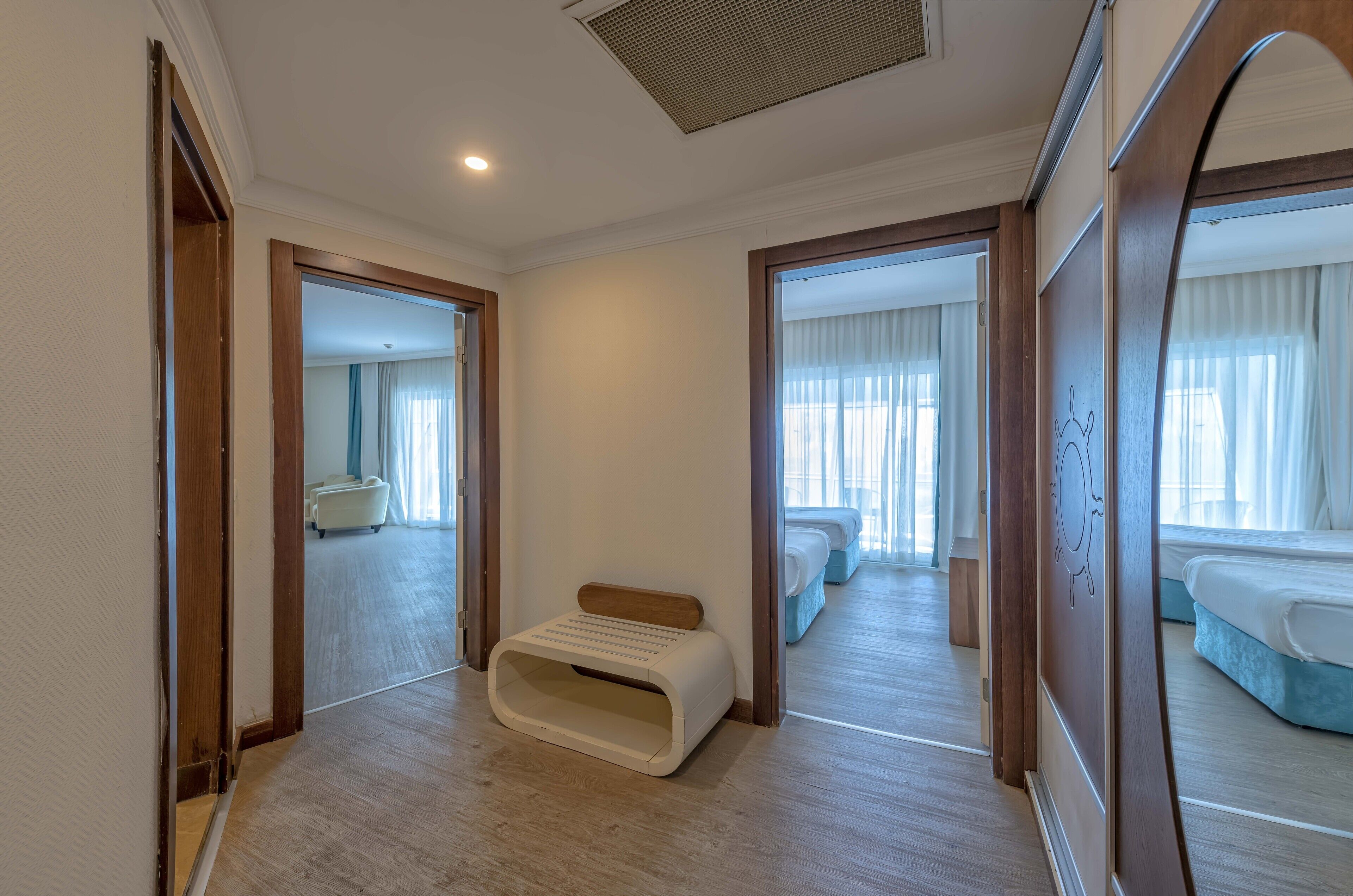 A hotel room with a wooden floor, a bench, and a bed with a blue headboard.