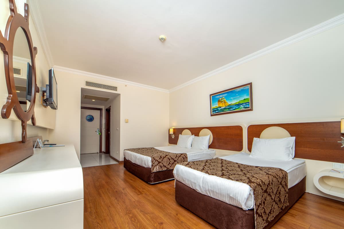 Ein Hotelzimmer mit zwei Betten, Holzboden, einem Gemälde an der Wand und einem Badezimmer mit Toilette und Waschbecken.