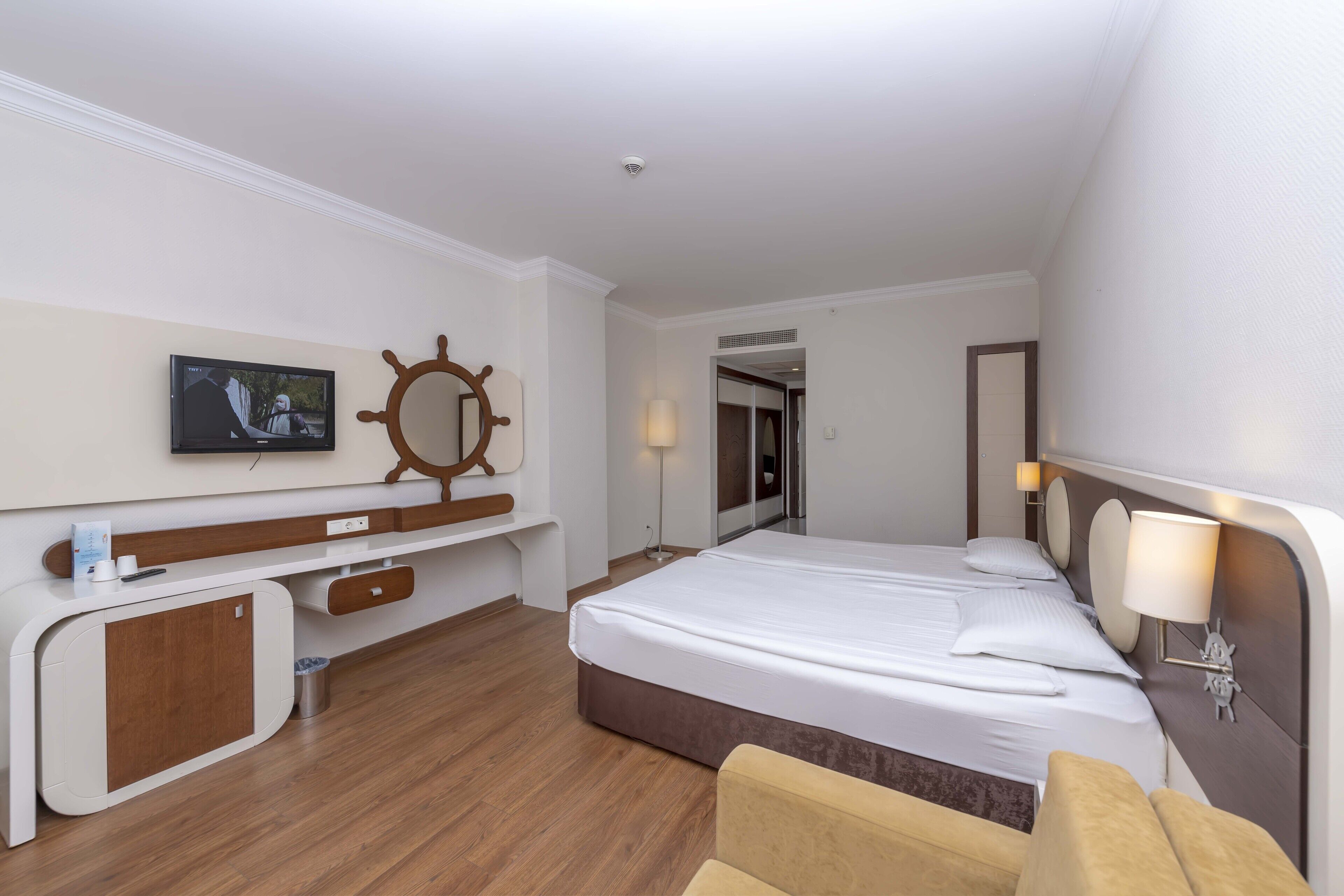 Una habitación de hotel con cama, escritorio, televisión, decoración de timón de barco y espejo.
