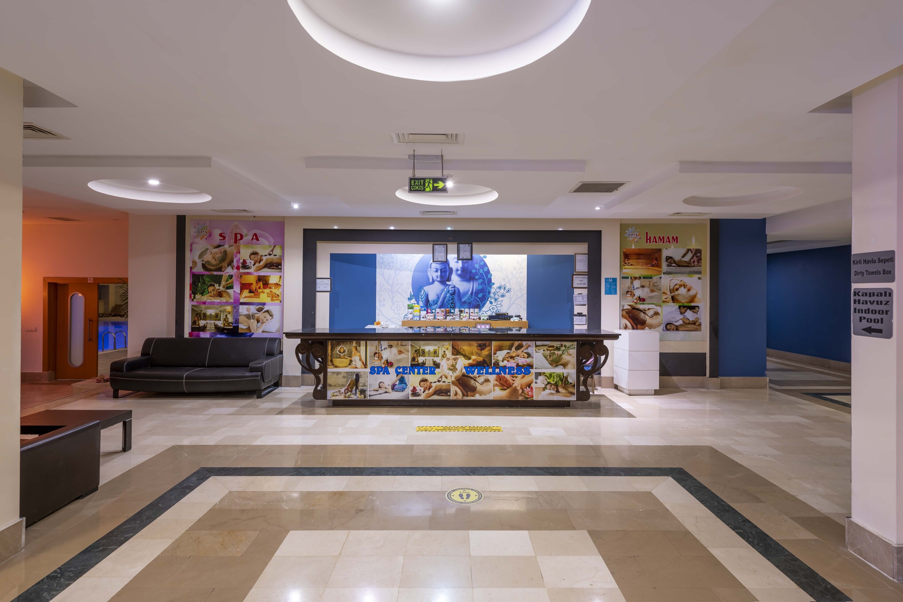 Eine Lobby mit einer Rezeption, einer Couch und einem Plakat, das Wellnessangebote bewirbt.