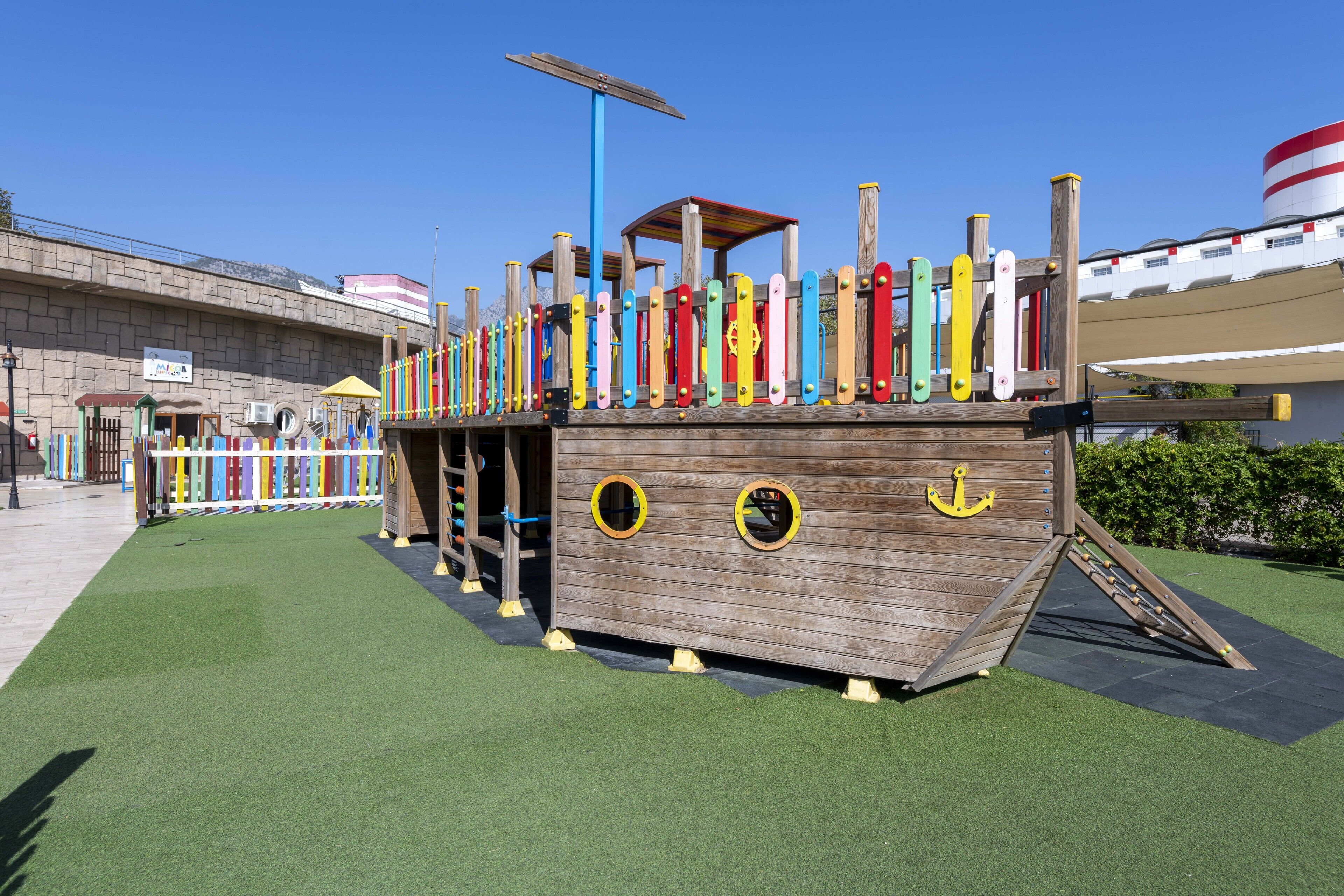 A wooden play structure resembling a pirate ship with a ramp and a small enclosed area.