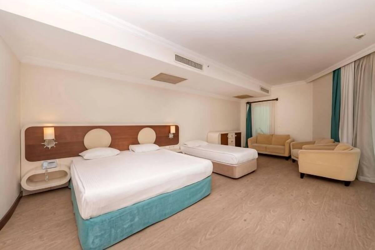 Ein Hotelzimmer mit einem großen Bett, zwei Nachttischen, einem Sofa und einem Fenster mit Vorhängen.