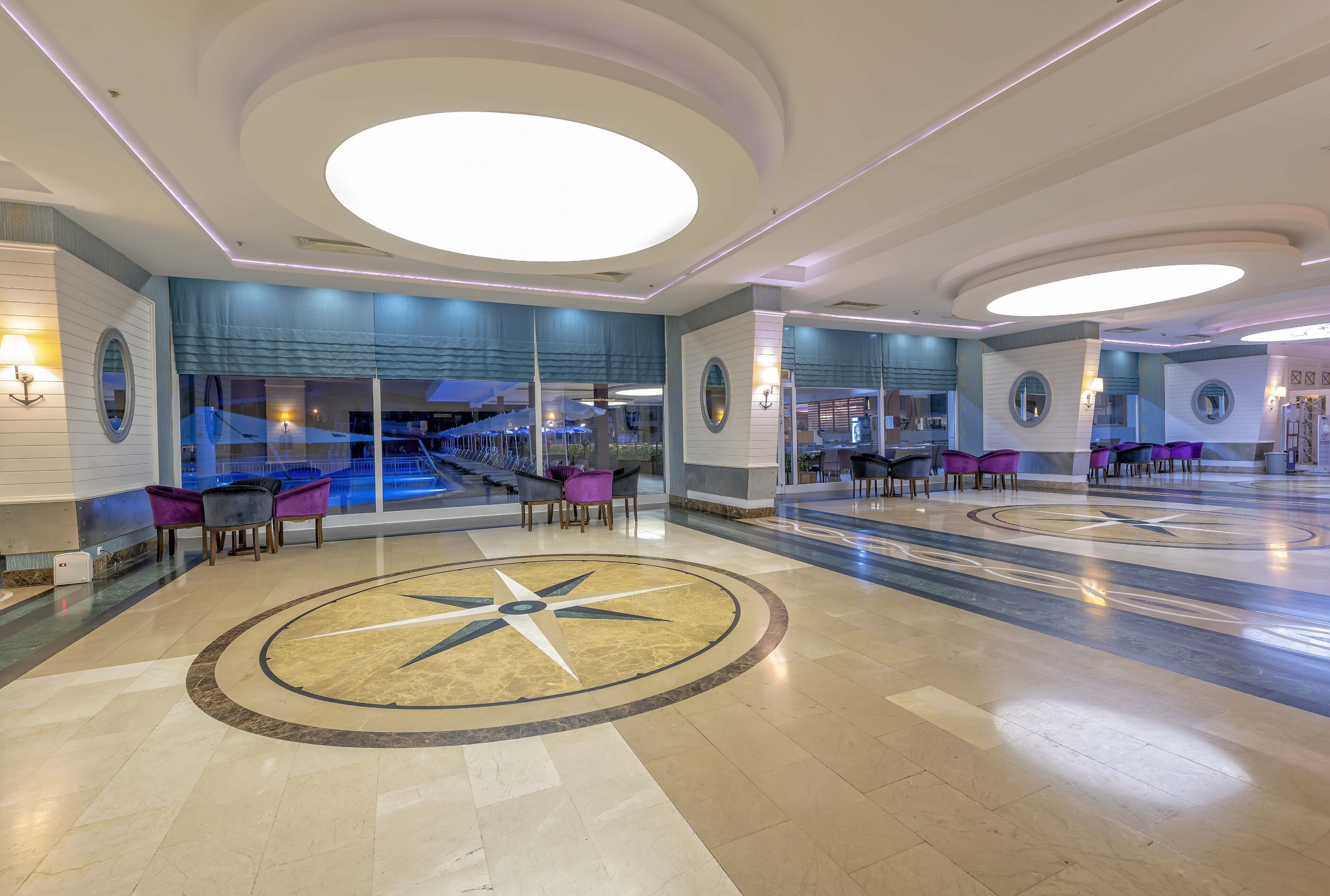 Um amplo hall de entrada com design circular central, áreas de estar e grandes janelas com vista para o exterior.