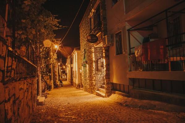 A narrow cobblestone street at night with stone buildings, a sign for 'PIRANTA', and a staircase leading to a second floor. - Pırlanta Butik Otel (Cesme)