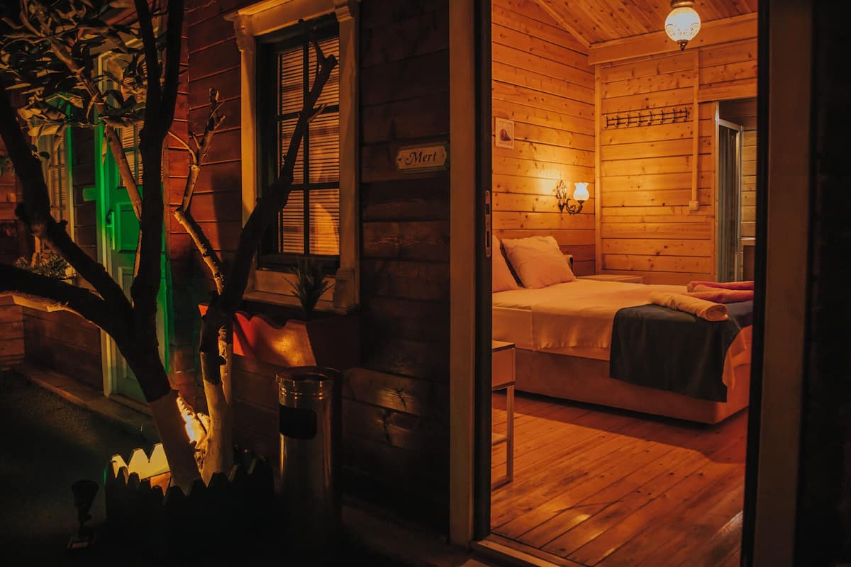 A cozy log cabin bedroom with a bed, a nightstand, and a wall-mounted lamp.