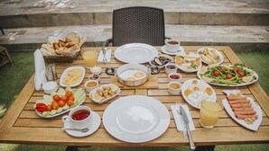 A wooden table set for breakfast with various dishes, including eggs, toast, and salad. - Pırlanta Butik Otel (Cesme)