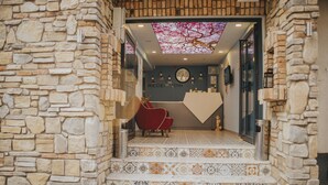 A reception area with stone walls, a tiled floor, a clock, and a red chair. - Pırlanta Butik Otel (Cesme)