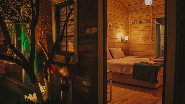 A cozy log cabin bedroom with a bed, a nightstand, and a wall-mounted lamp. - Pırlanta Butik Otel (Cesme)