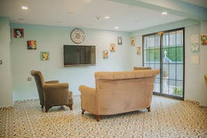 A room with a patterned floor, a sofa, a chair, and a television on the wall. - Pırlanta Butik Otel (Cesme)