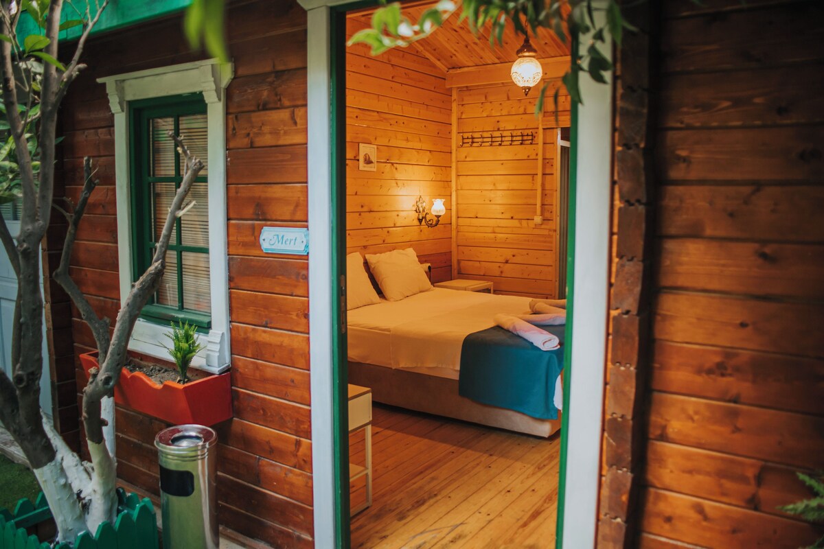 Una cabaña de madera con una cama, una mesita y una lámpara fijada a la pared.
