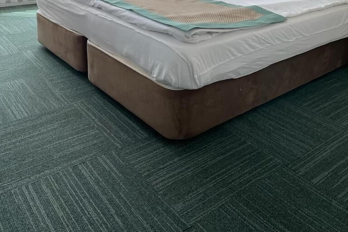 A hotel room with a large bed, a headboard, a wall-mounted air conditioner, and a framed picture above the bed.