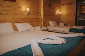 A hotel room with two beds, wooden walls, and a small table with a vase of flowers. - Pırlanta Butik Otel (Cesme)