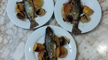 Tres platos de pescado a la parrilla y patatas asadas sobre una encimera de mármol.
