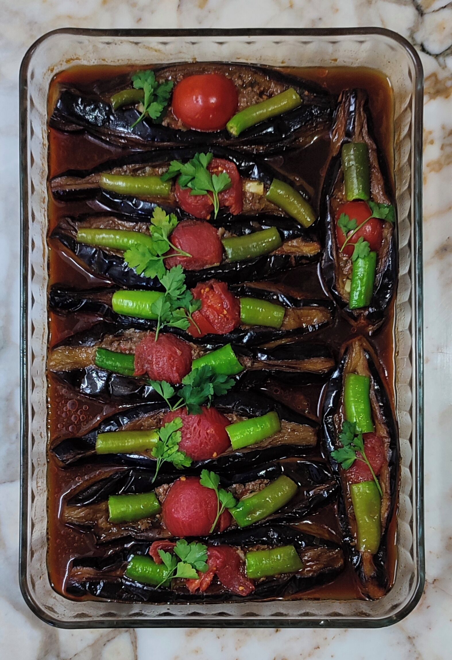 Una pirofila di vetro con melanzane, peperoni verdi, pomodori e prezzemolo arrostiti.