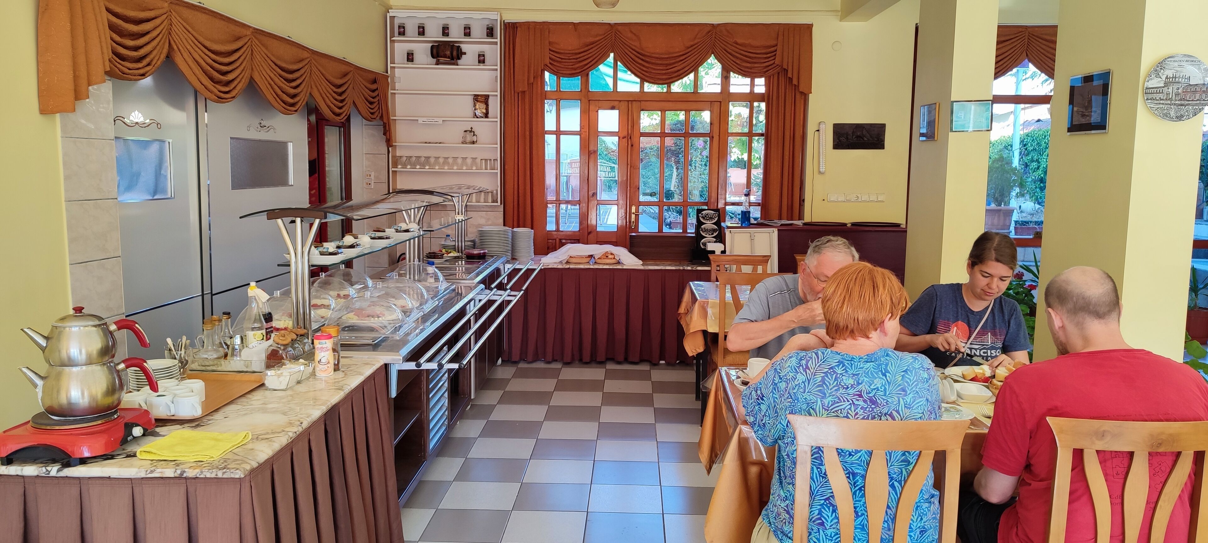 A dining area with a buffet setup, a counter with kitchen appliances, and a window with curtains.