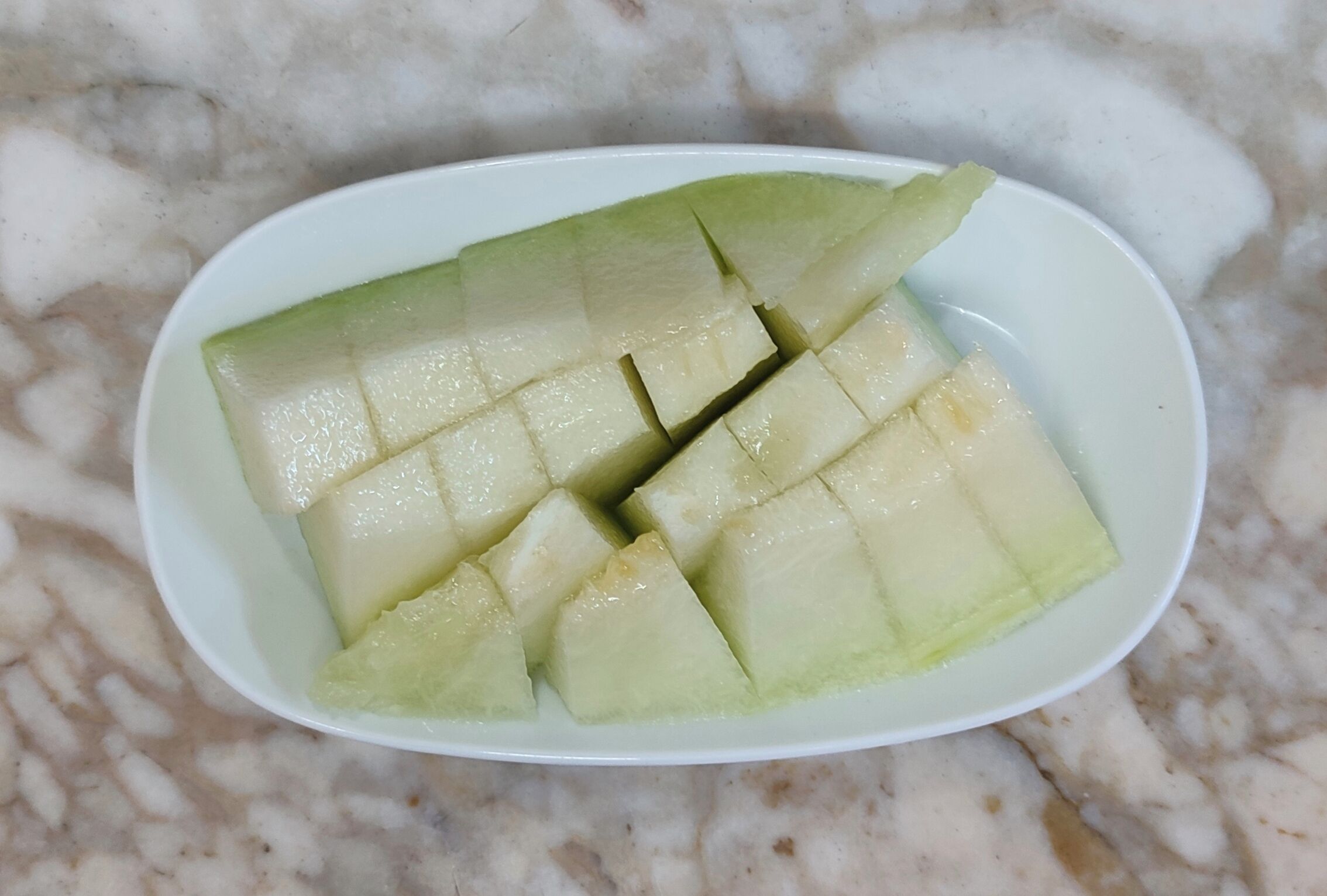 Un plato blanco con fruta en cubos sobre una encimera de mármol.