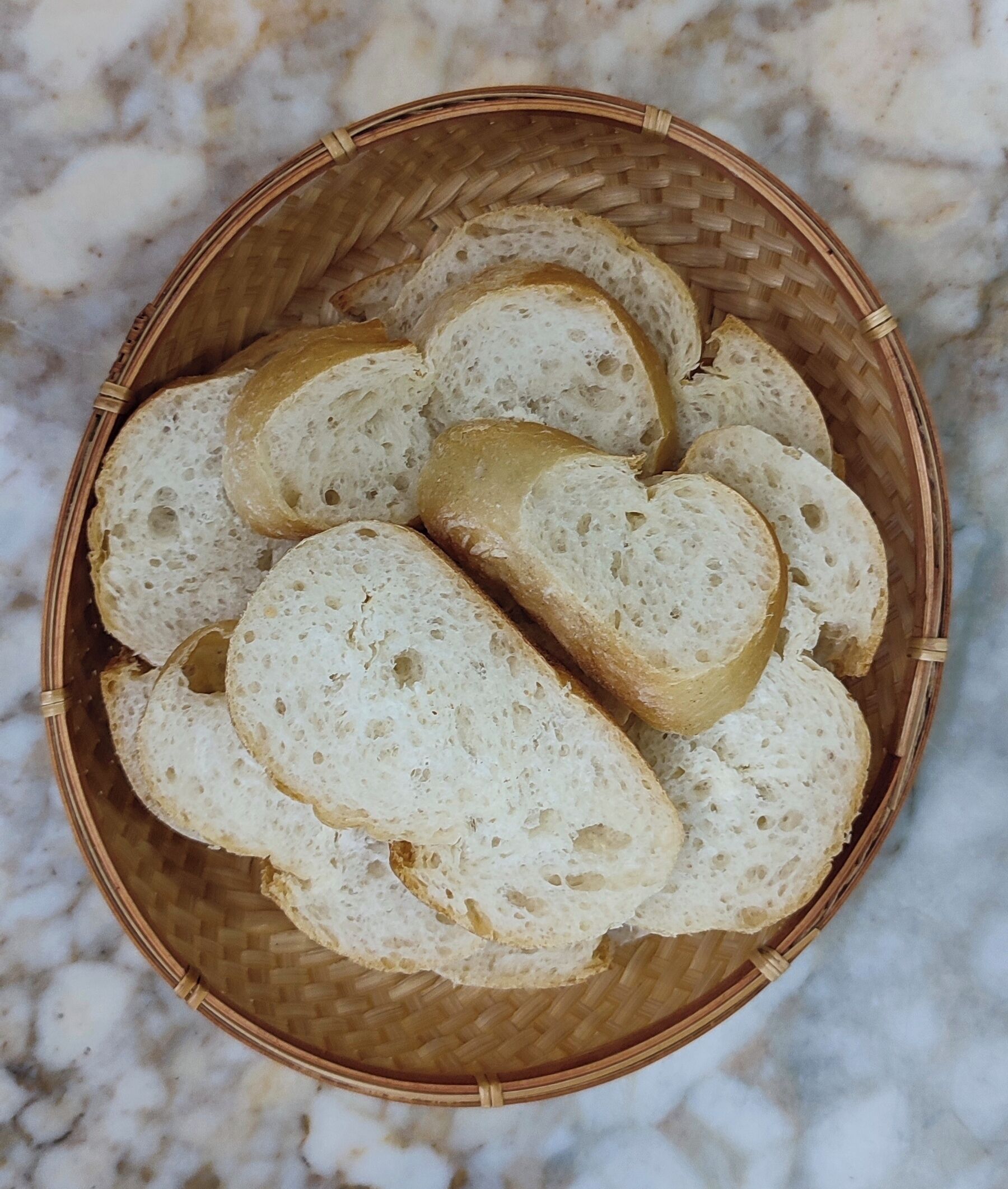 A basket containing several slices of white bread on a marble surface.