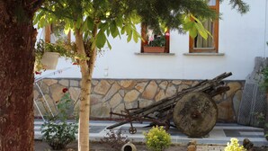 A stone wall with a large wheel, a tree, and a small garden with various plants. - Hotel Baykal (Bogazkale)