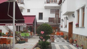 A hotel courtyard with outdoor seating, a central garden with flowers, and a red awning. - Hotel Baykal (Bogazkale)