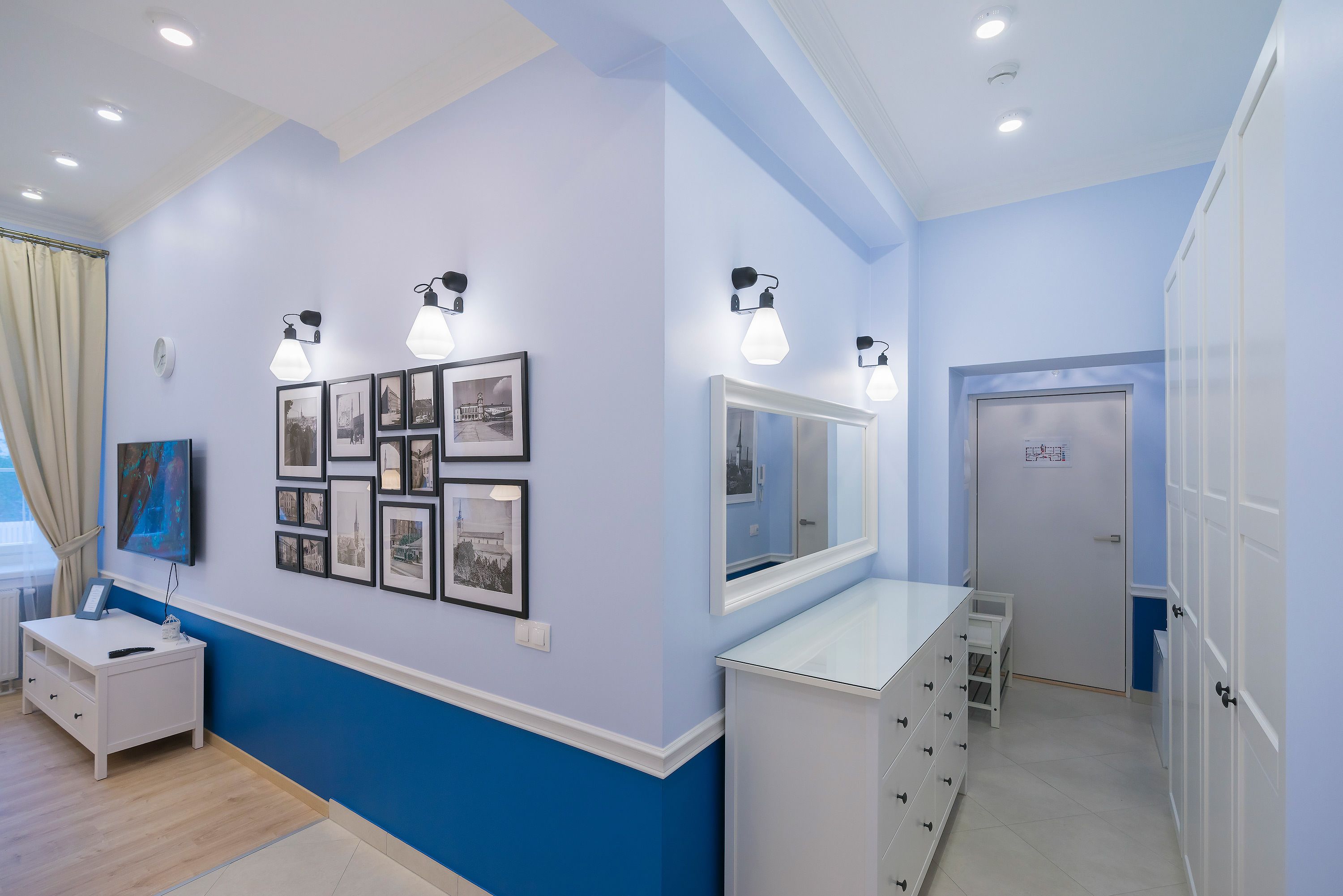 A room with a blue and white color scheme, featuring a white dresser, a vanity with a mirror, and wall-mounted picture frames.