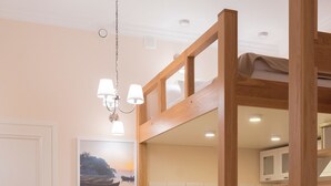 Un interior moderno con una escalera de madera, una zona de comedor con sillas blancas y una cocina al fondo.
