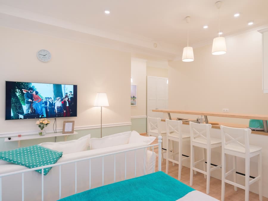 A hotel room with a TV, a crib, a dining area with chairs, and a kitchen counter.