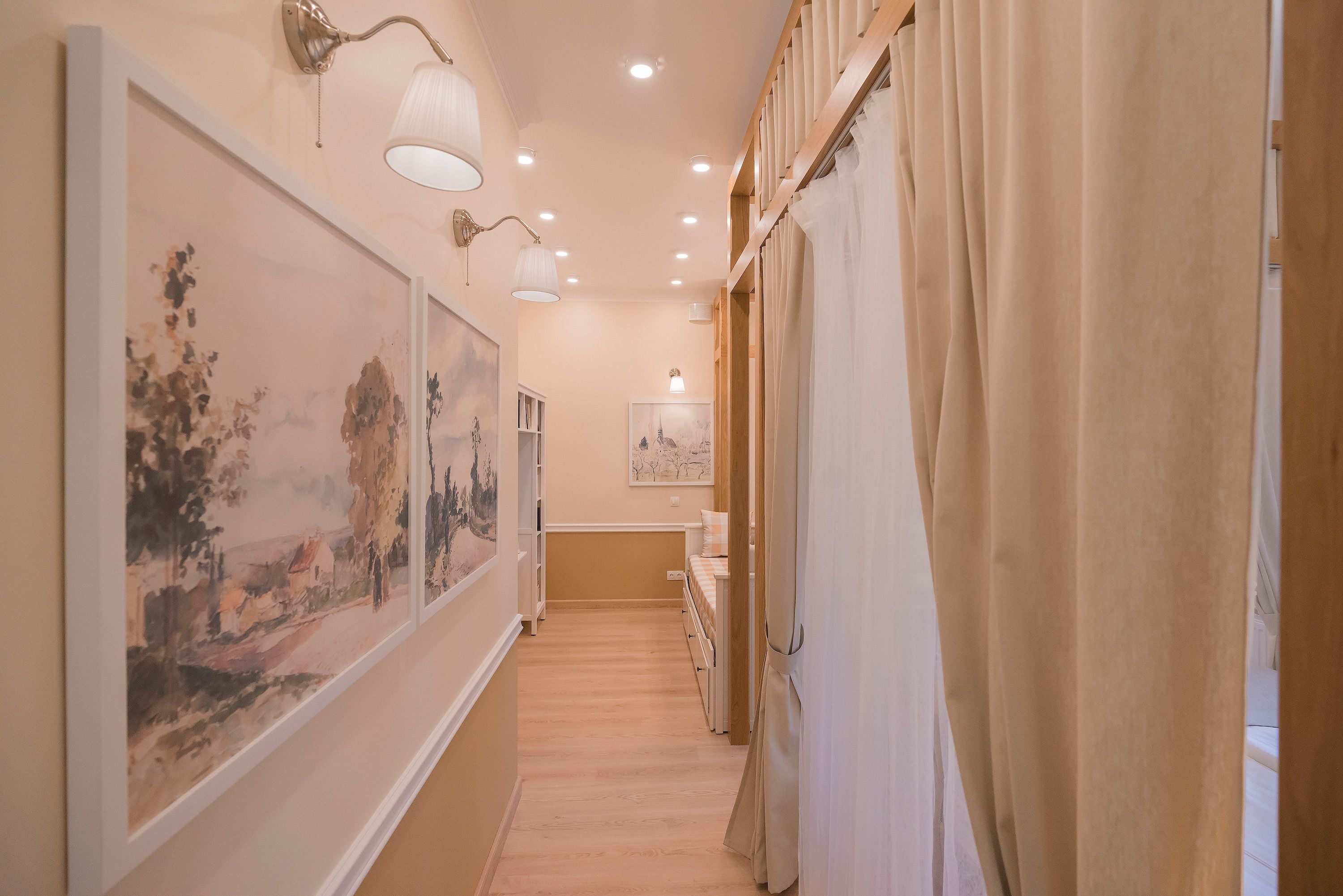 Un pasillo con obras de arte en las paredes, piso de madera y una cama con cabecera blanca al fondo.