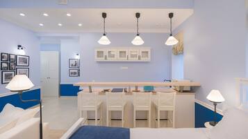 A bedroom with a bed, bedside tables, a desk, and chairs. There is a kitchenette with cabinets and a countertop.