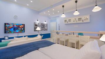 A modern hotel room with a large bed, bedside tables, a desk, and a chair. There is a television mounted on the wall, a clock, and framed pictures.