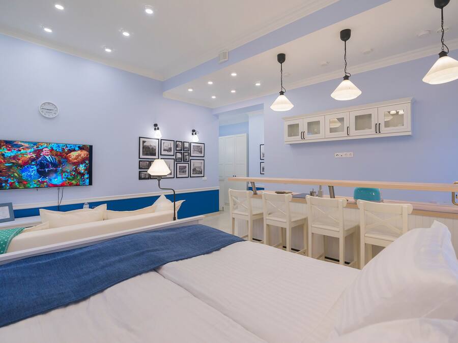 Ein modernes Hotelzimmer mit einem großen Bett, Nachttischen, einem Schreibtisch und einem Sessel. An der Wand ist ein Fernseher befestigt, daneben eine Uhr und gerahmte Bilder.