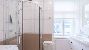 A modern bathroom with a glass-enclosed shower, white tiles, a window with a view, and a white sink.