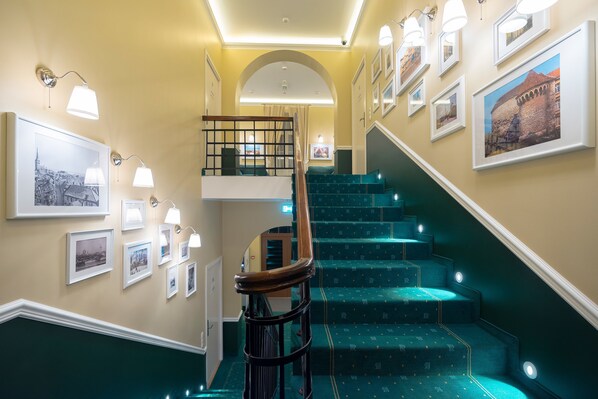 A staircase with green carpeted steps, a wooden handrail, and wall-mounted picture frames.