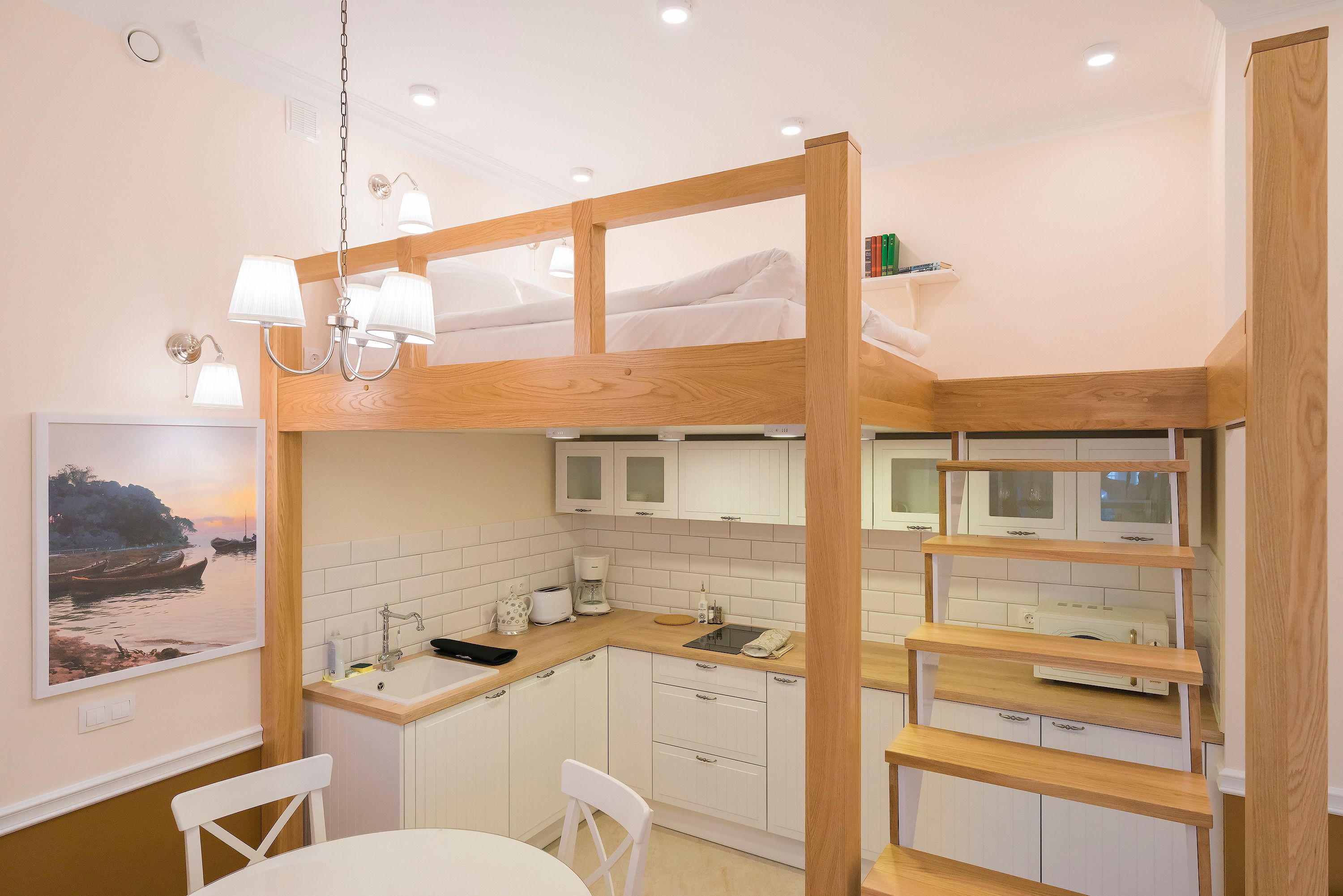 A compact kitchen with white cabinets, a wooden counter, and a bunk bed with white bedding.