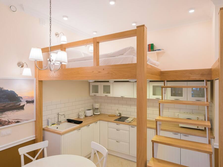 A compact kitchen with white cabinets, a wooden counter, and a bunk bed with white bedding.