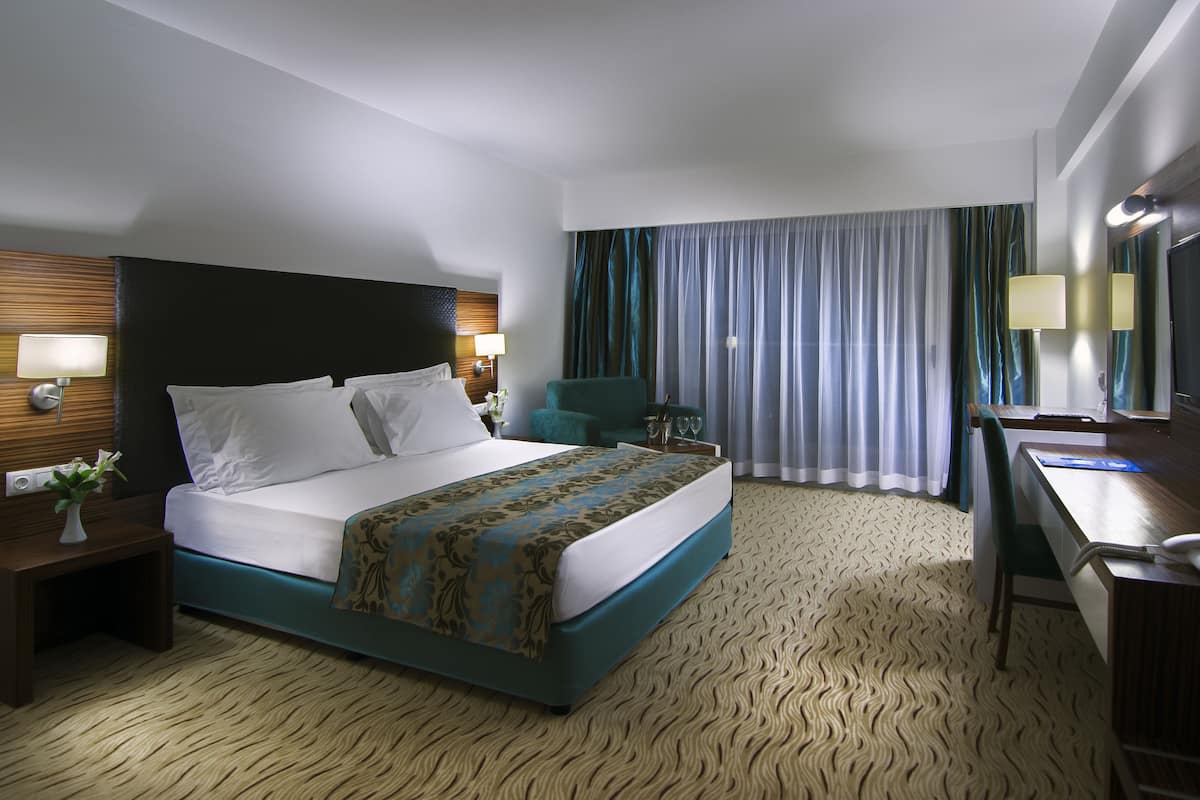 Une chambre d’hôtel avec un grand lit, un bureau, une chaise, une salle de bain et une fenêtre avec des rideaux.