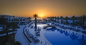 A resort pool area with lounge chairs, umbrellas, and a sunset view.