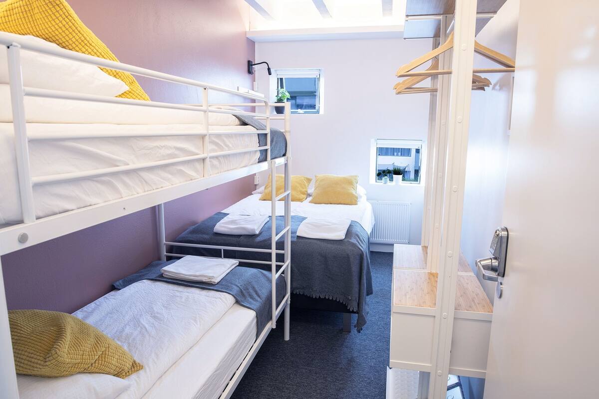 Ein Schlafsaalzimmer mit Etagenbetten, einem kleinen Fenster und einer Heizung.