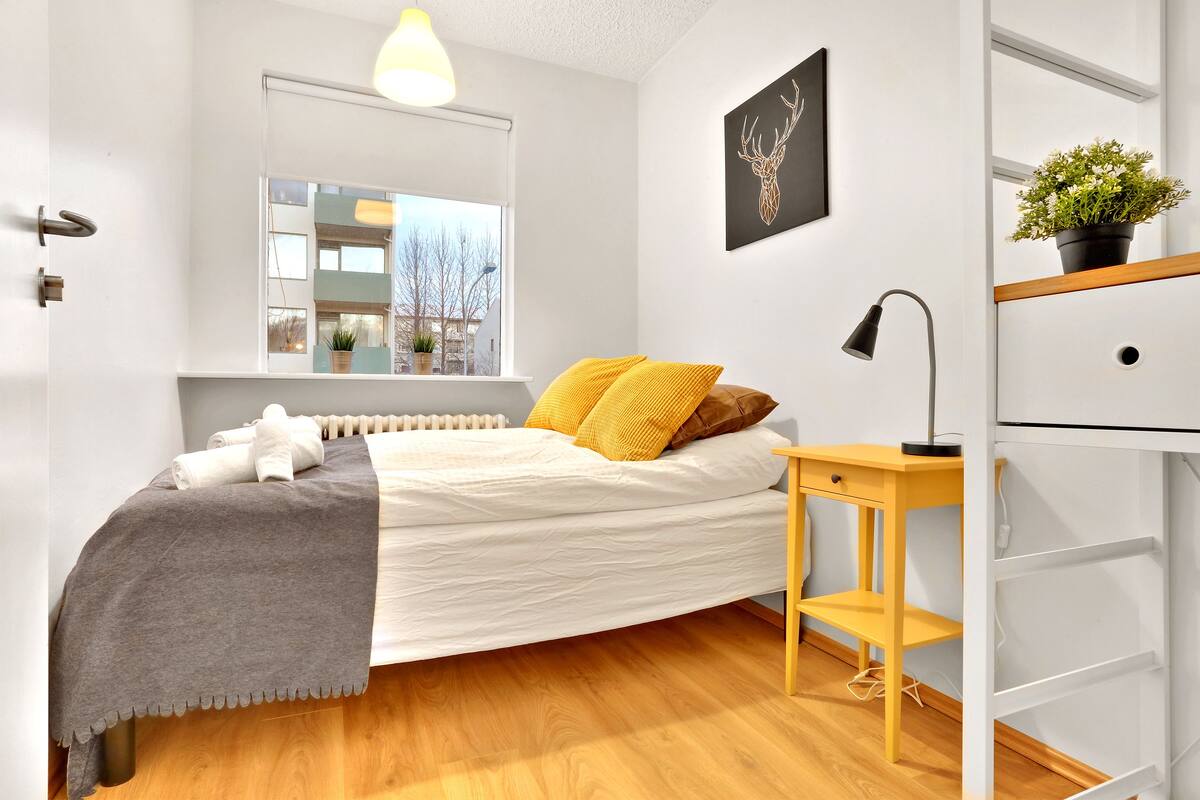Ein modernes Schlafzimmer mit Bett, Nachttisch, Lampe, Heizkörper, Fenster und Pflanze.