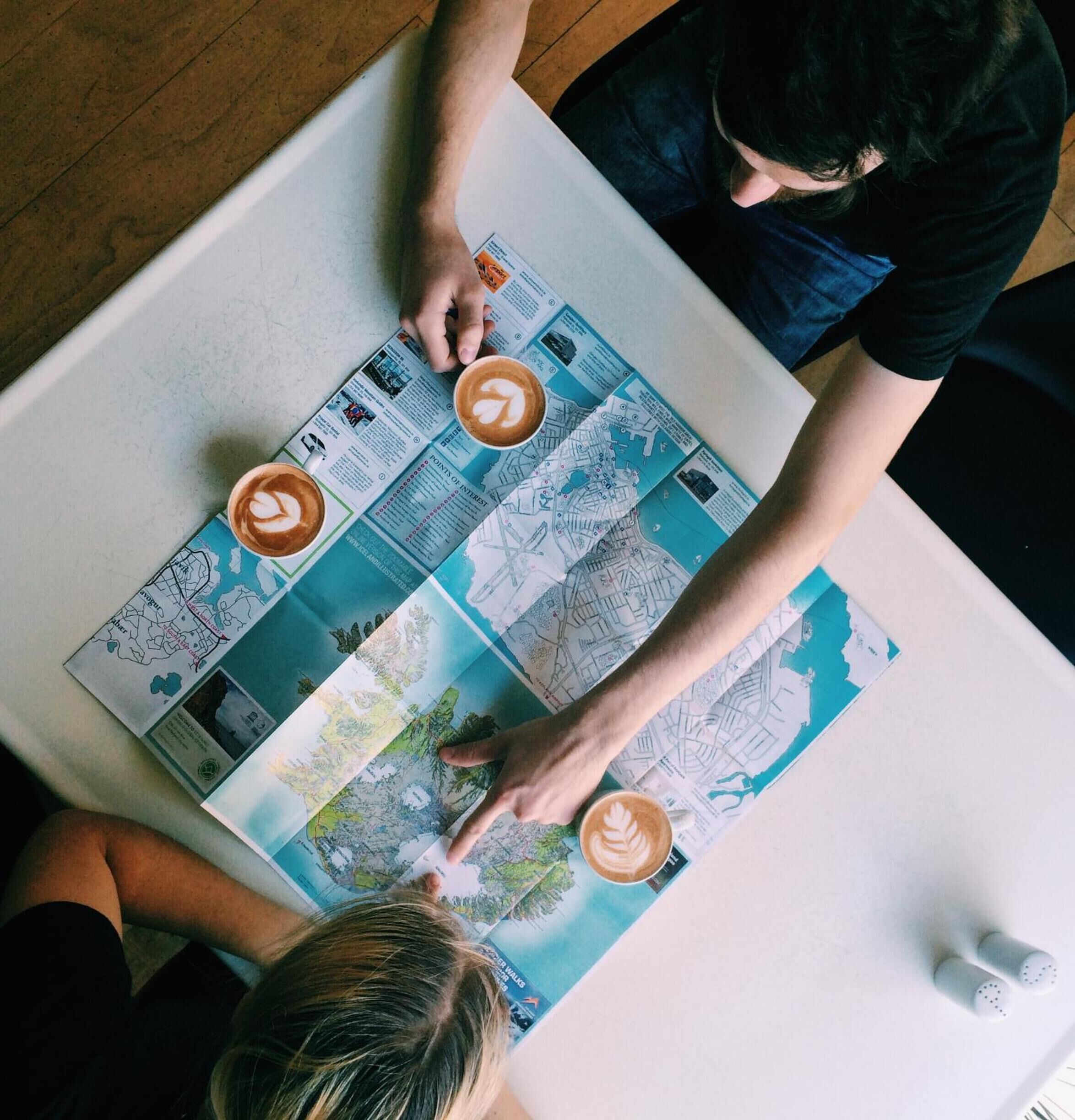 A person pointing at a map with coffee cups on a table.