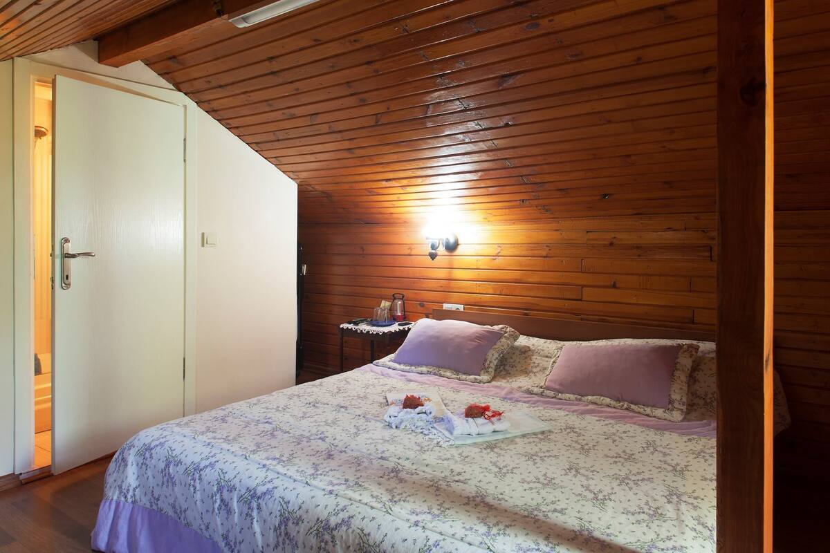 Un dormitorio con techo de madera, una cama con ropa de cama floral, una mesita de noche con lámpara y un armario.
