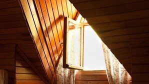 Un dormitorio acogedor en el ático con paredes de madera, techo inclinado y ventana con cortinas florales.