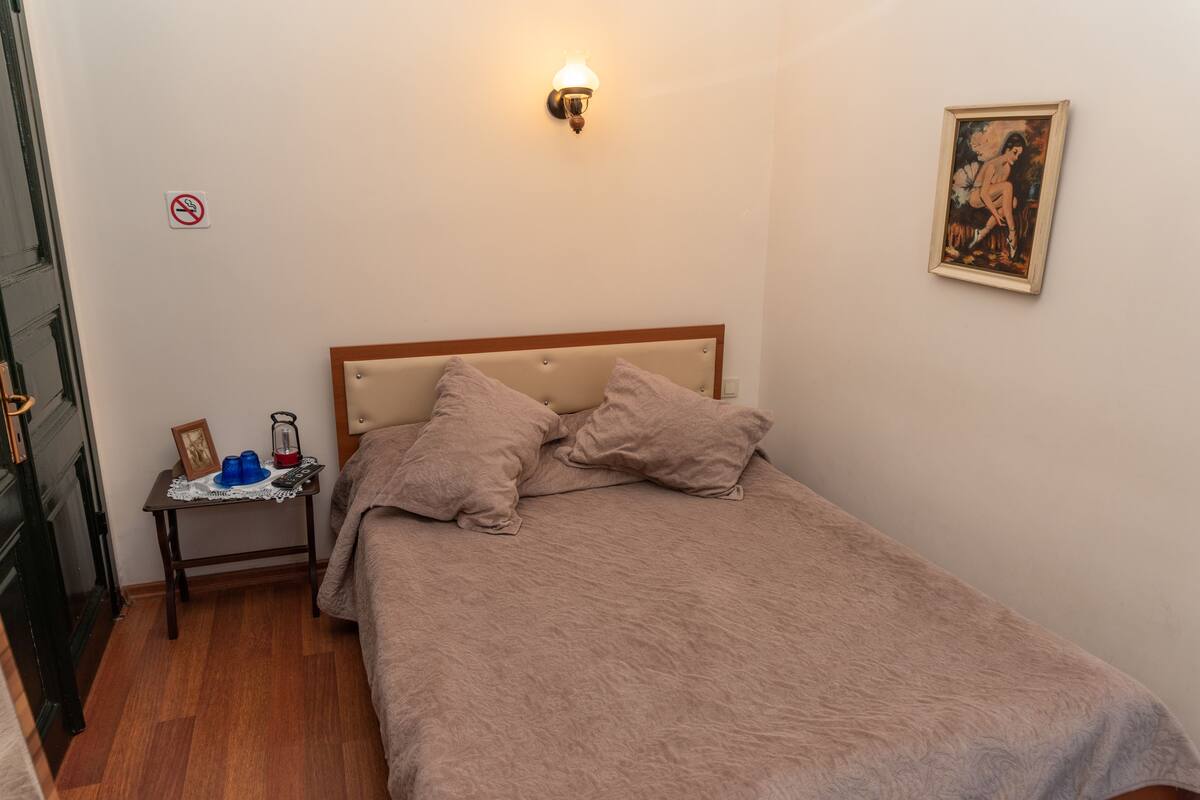 Un dormitorio con cama, mesita de noche, lámpara de pared, cuadro enmarcado y una puerta.