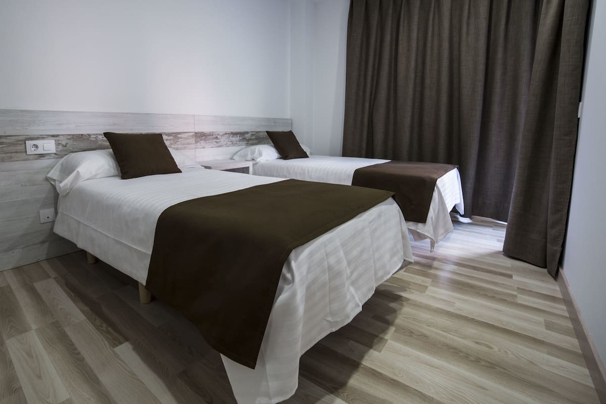 A hotel room with two beds, a wooden headboard, a brown throw blanket, and a curtain.