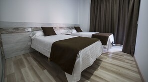 A hotel room with two beds, a wooden headboard, a brown throw blanket, and a curtain. - Apartaments Ponent (Lloret de Mar)