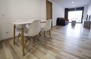 A modern living room with a dining area, featuring a wooden floor, white chairs, a sofa, and a TV.
